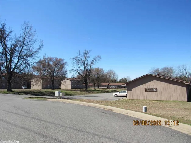 A far-away view of the Cedar Creek Apartment complex, managed by Welcome Home Properties. The buildings are small and rectangular and made of brown siding. There appear to be several that stretch far back from the road. The time stamp is 03/06/2020/ 12:12.